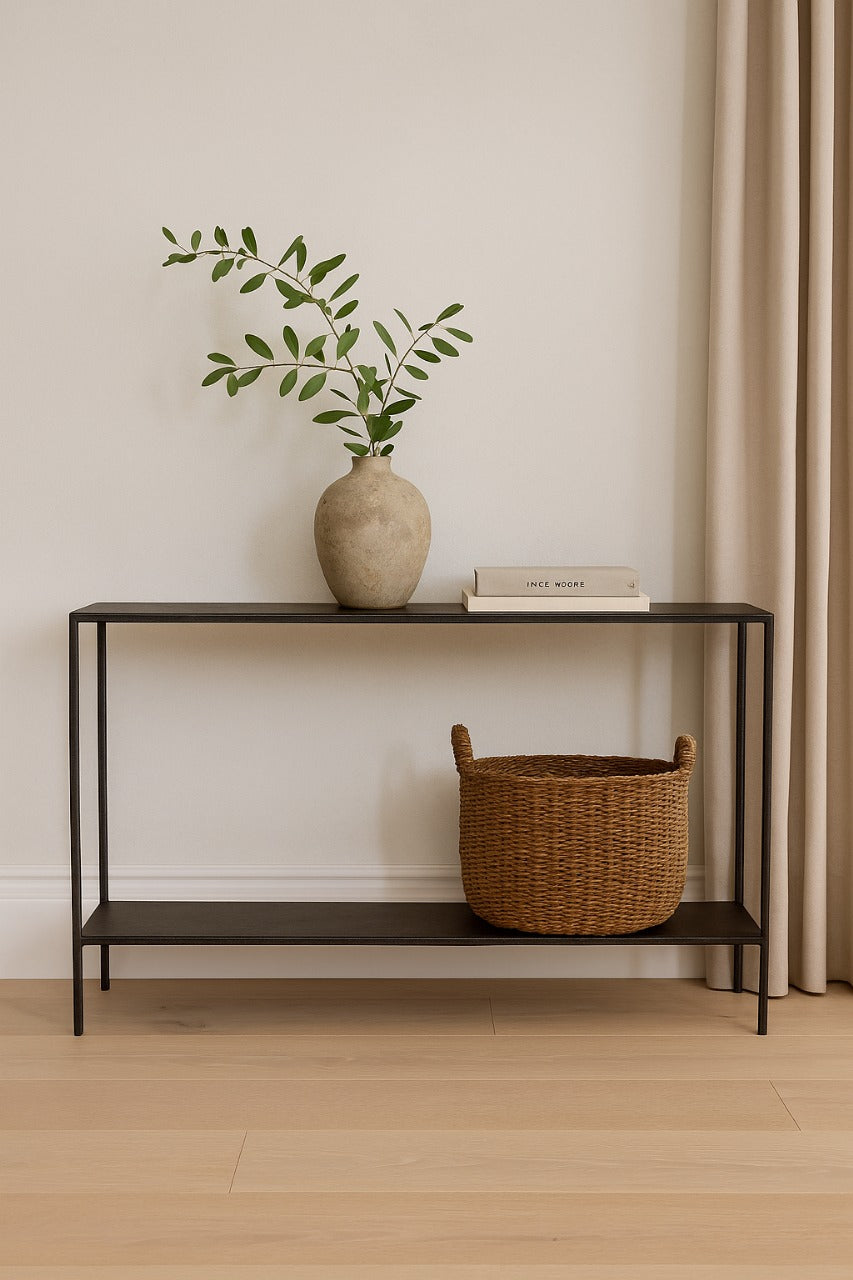 Console table with a vase, books, and basket against a beige wall.