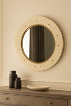Round mirror with decorative frame on a wall above a wooden dresser.
