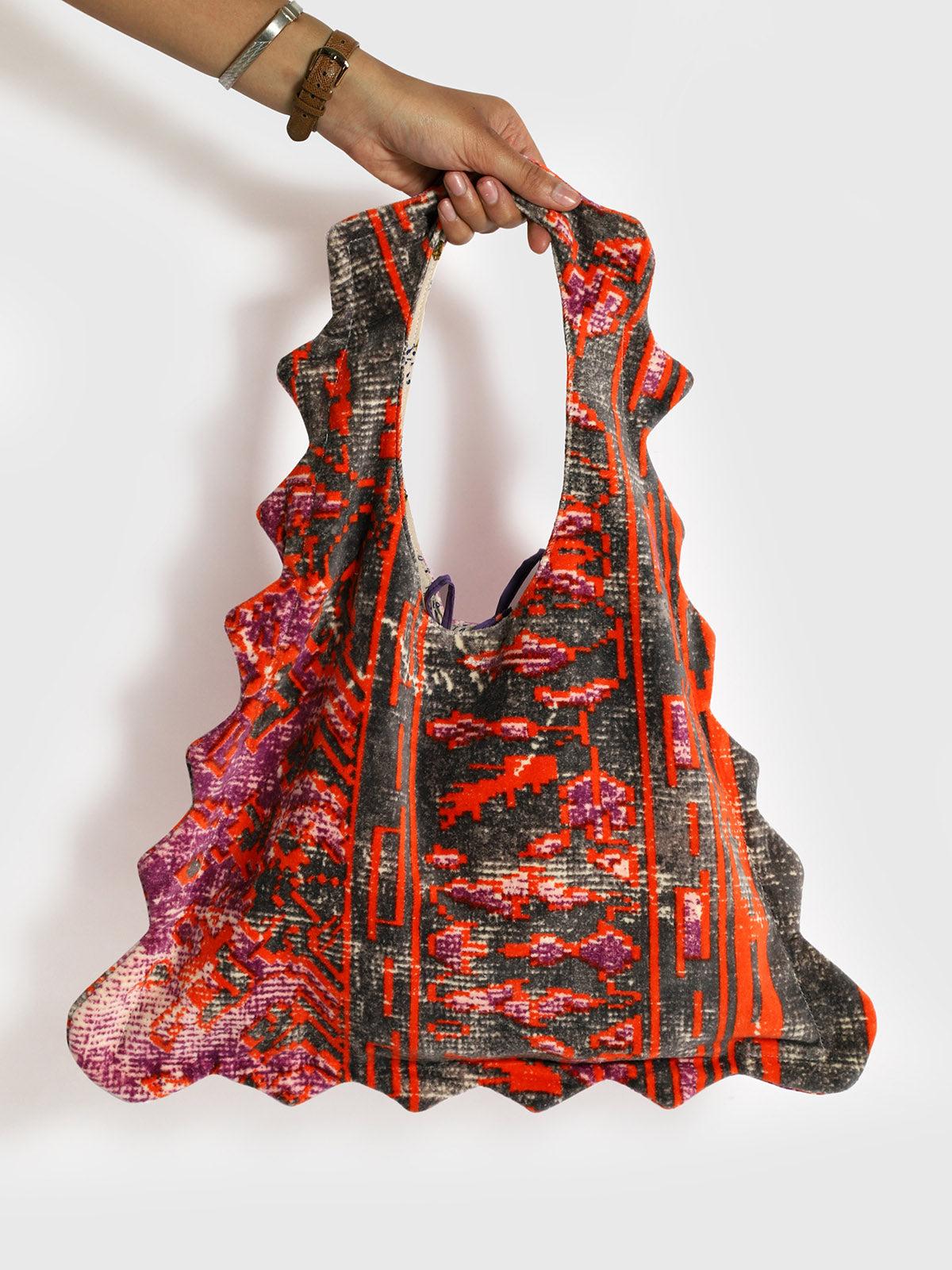 Colorful patterned velvet tote bag held by a hand on a white background